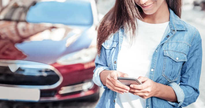 Woman searching on phone standing in front of a car